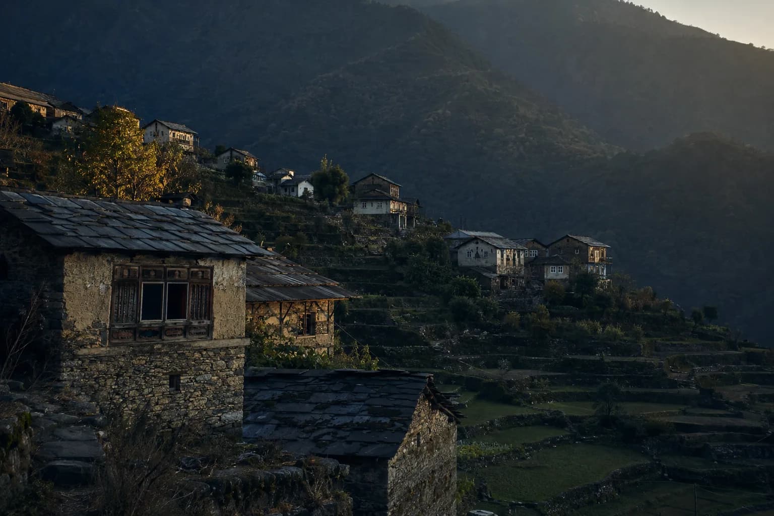Slate-roofed houses on a terraced hillside, forested ridges behind